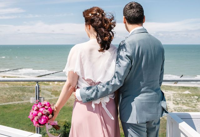 Hochzeitspaar mit Blumenstrauß blickt von Terrasse auf die Ostsee.