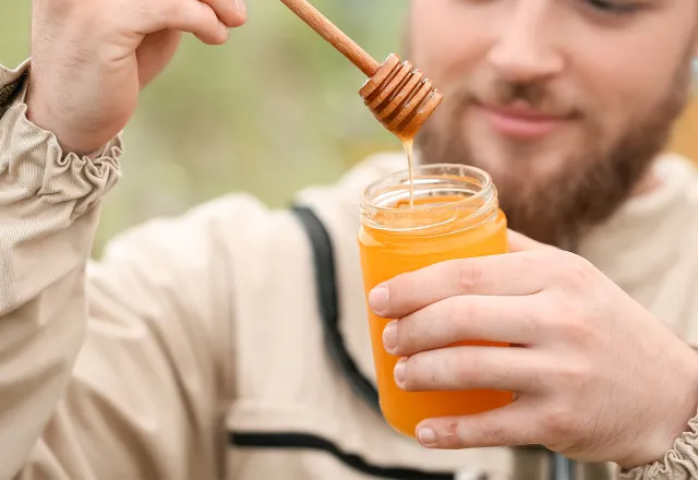 Ein Imker, der ein Glas Honig mit einem Honiglöffel in der Hand hält. ©Adobe Stock, Pixel-Shot