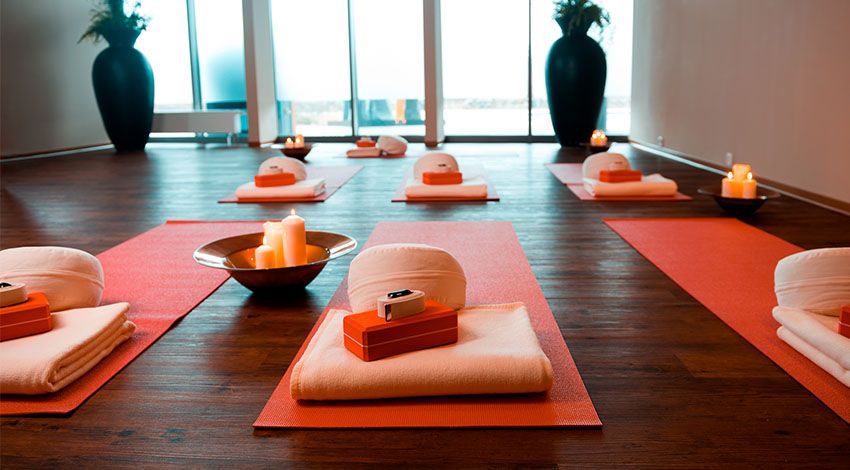 Yogaraum des THE GRAND Ahrenshoop mit orangefarbenen Matten, weißen Kissen und Kerzen, die eine ruhige Atmosphäre schaffen.