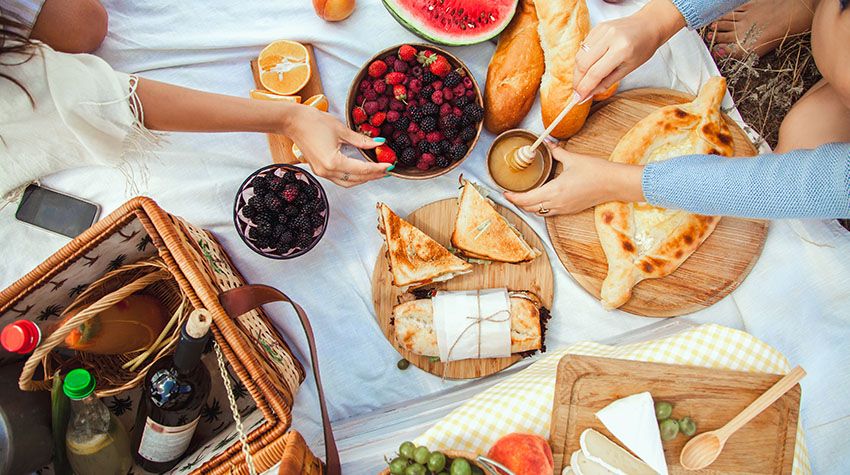 Bunte Picknicktafel mit frischen Früchten, Gebäck und Getränken auf einer Decke im Freien.