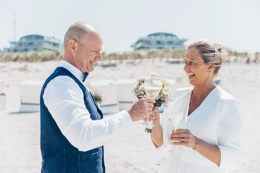Brautpaar stößt mit Sektgläsern am Strand vor den Dünen in Ahrenshoop an.