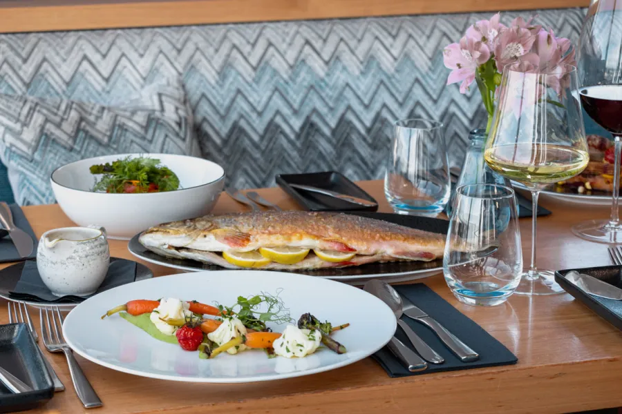 Gebratener Fisch mit Beilagen und Wein wird im Restaurant WEITBLICK in Ahrenshoop serviert.
