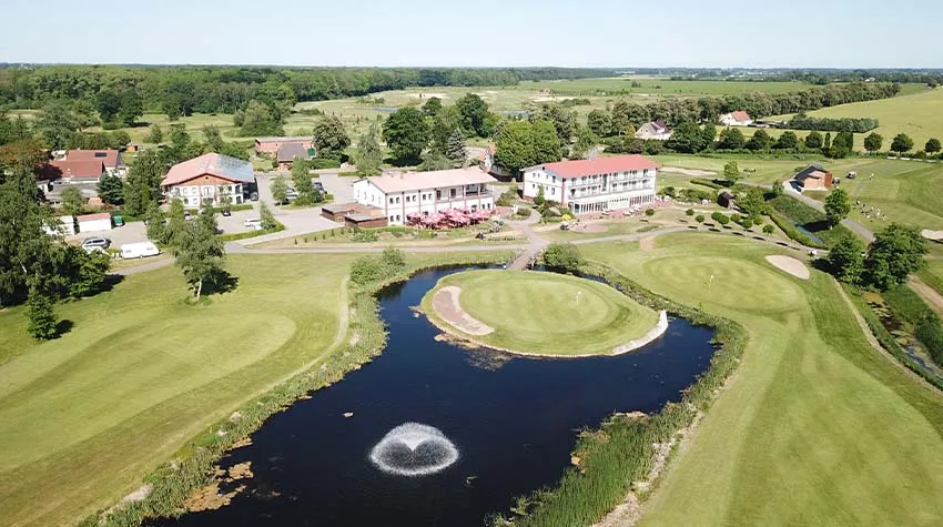 Luftaufnahme der weitläufigen Golfparkanlage Strelasund mit Gasthaus, Teich und mehreren Golfplätzen.