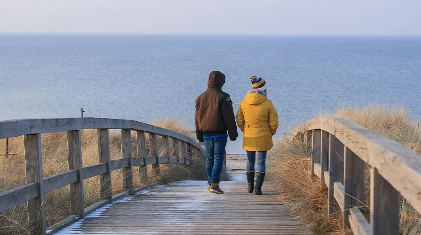 Mutter und Sohn spazieren über eine Holzbrücke entlang der Ostsee. © Adobe Stock, Lars Gieger