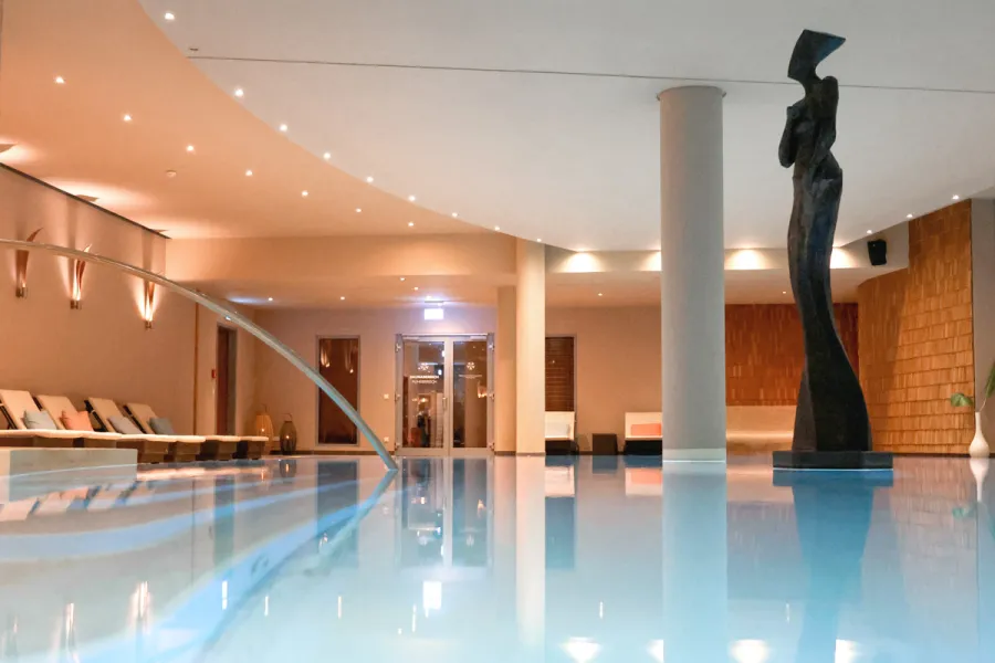 Innenpool im Spa-Bereich des THE GRAND Ahrenshoop mit Liegen und Skulptur.