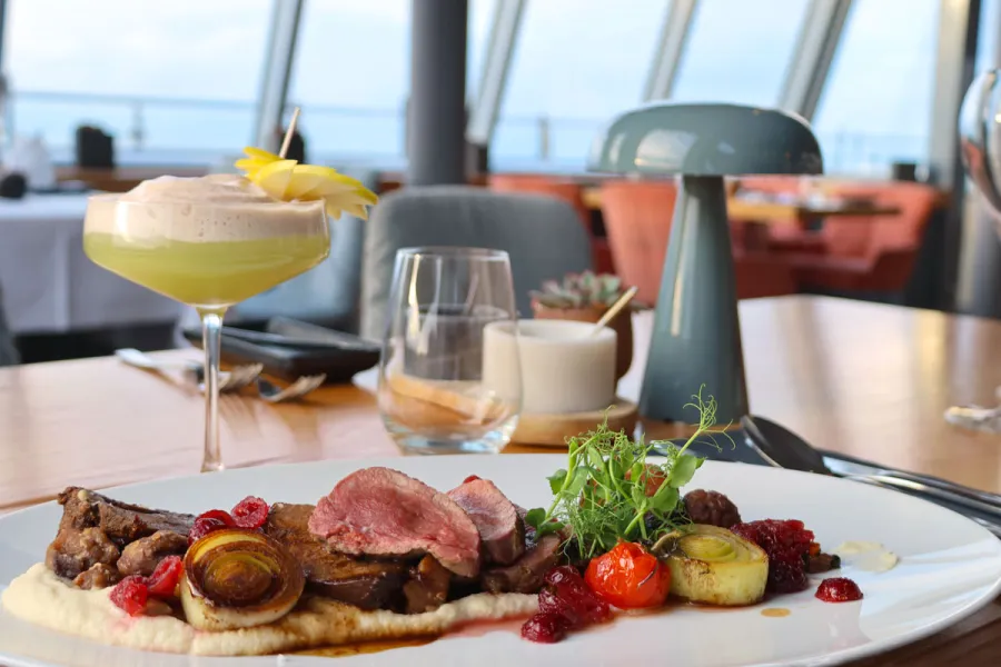 Angerichtetes Fleischgericht mit Cocktail wird im Restaurant WEITBLICK mit Blick auf die Ostsee serviert.