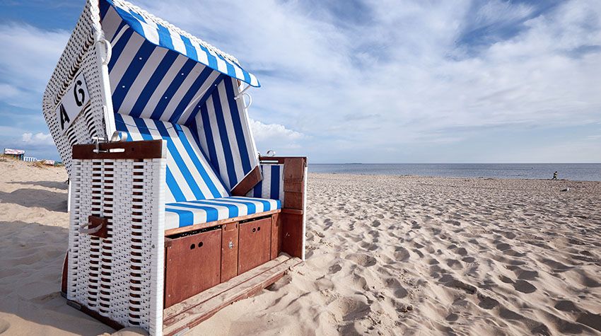 Klassischer Strandkorb mit blau-weißen Streifen direkt am Ostseestrand bei Sonnenschein.