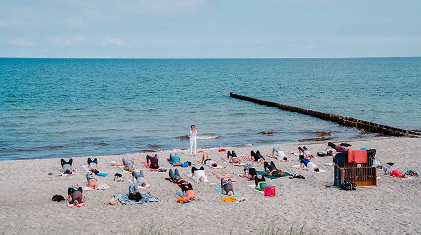 Eine Gruppe Menschen praktiziert Yoga auf bunten Matten am Strand der Ostsee.