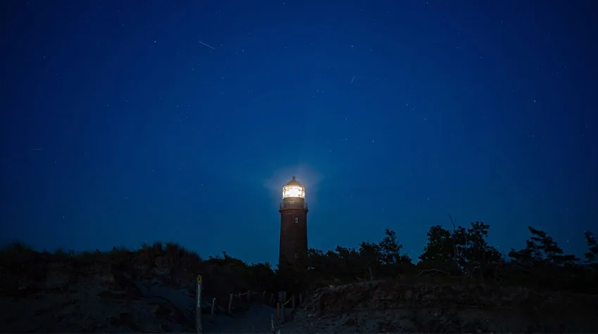 Leuchtturm Darßer Ort in einer dunklen Nacht mit klarem blauen Himmel.