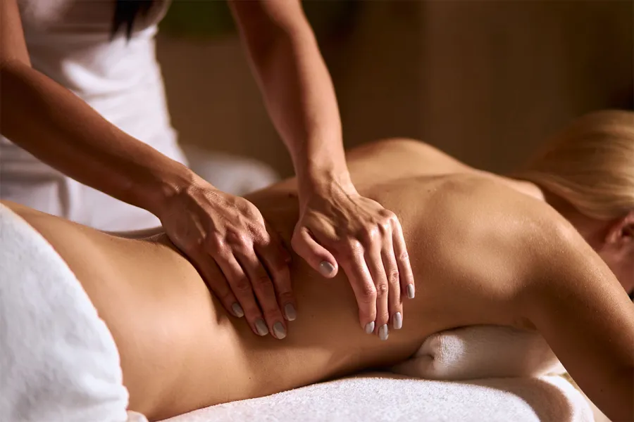 Eine Frau liegt entspannt auf der Liege, während eine Masseurin ihren Rücken mit sanften Griffen massiert.