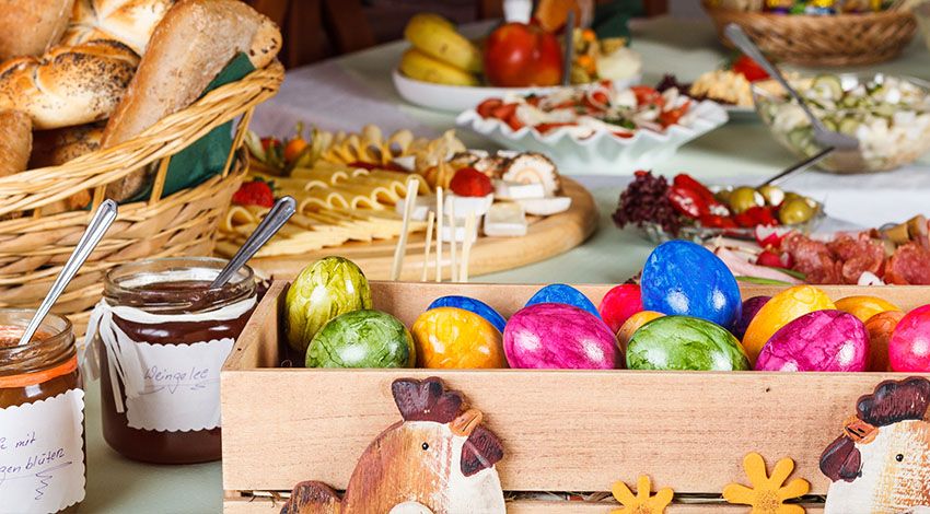 Ein Osterbrunch mit bunten Eier im Mittelpunkt, begleitet von einer Auswahl an Aufschnitt und frisch gebackenem Gebäck.
