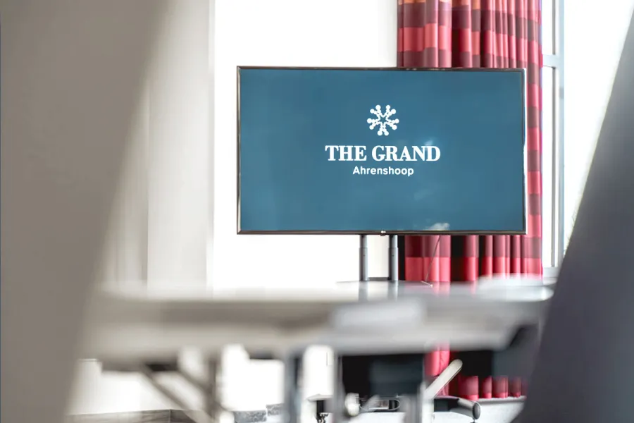 Monitor mit Logo von THE GRAND Ahrenshoop in einem hellen Tagungsraum.