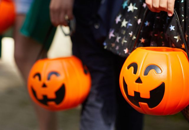 Kinder mit Halloween-Kürbiseimern gehen verkleidet von Haus zu Haus, um Süßigkeiten zu sammeln.