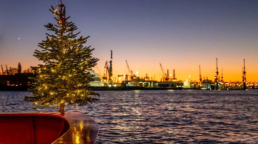 Ein Tannenbaum an der Spitze eines Schiffs, im Hintergrund der Hamburger Hafen.