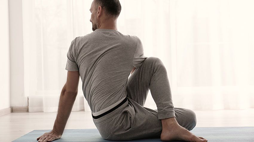 Ein Mann sitzt auf einer Yogamatte und dreht sich in eine sanfte Dehnposition.