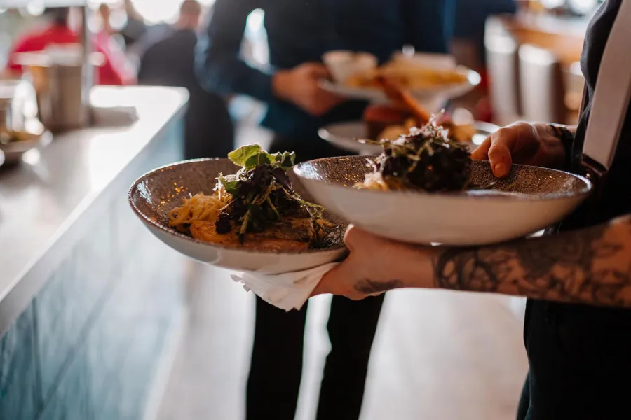 Servicekraft trägt mehrere angerichtete Teller durch den Restaurantbereich des THE GRAND Ahrenshoop.