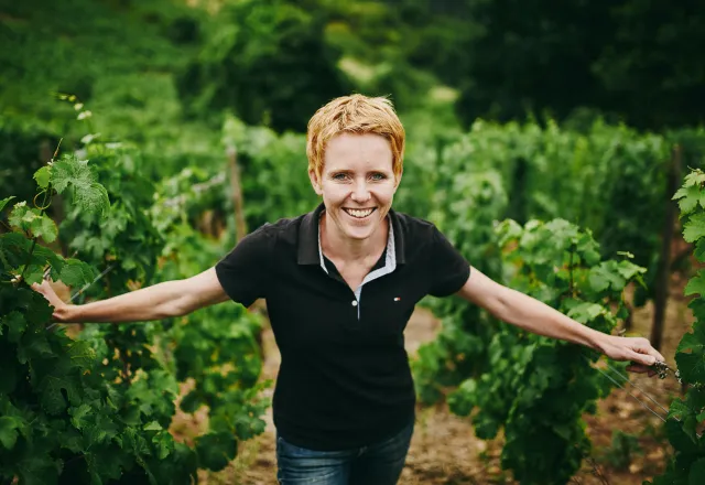Winzerin Anette Closheim, die in einem Feld voller Weintraubenreben steht und lächelt. ©Anette Closheim
