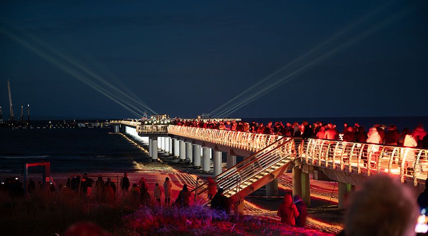 Die Seebrücke in Prerow bei Abenddämmerung, hell beleuchtet und umringt von Menschen.
