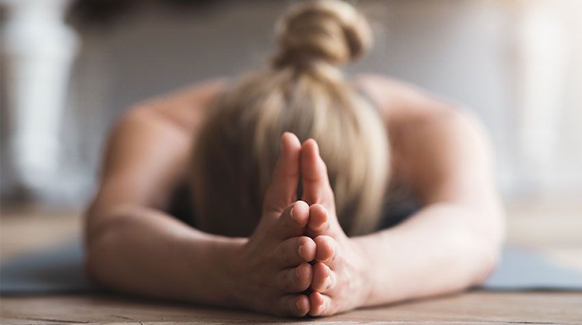 Eine Frau liegt auf einer Yogamatte und beugt sich nach vorn, um sich bewusst zu entspannen.