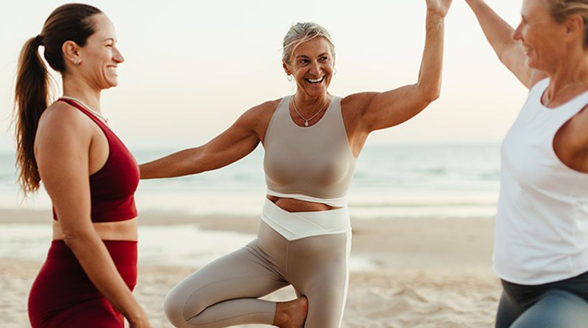 rei Frauen stehen lachend am Strand der Ostsee und genießen die gemeinsame Yogastunde.