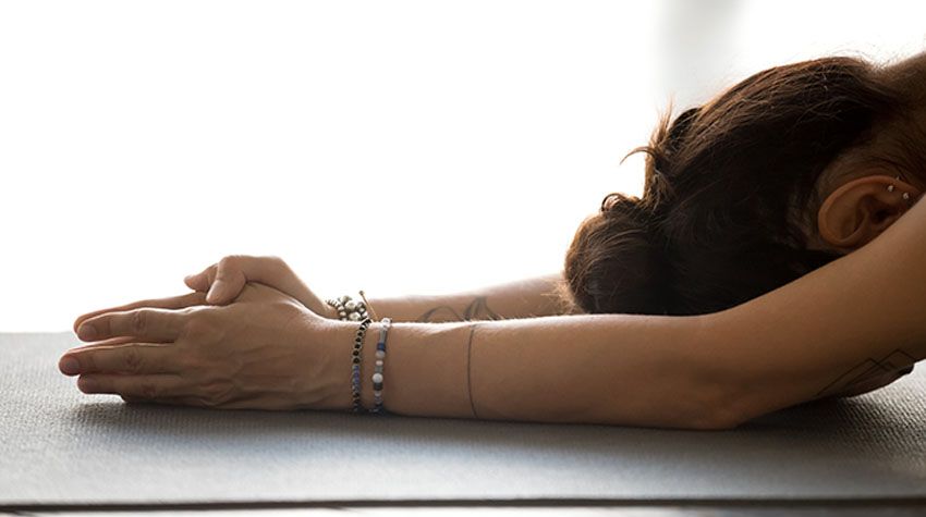 Eine Frau liegt auf einer Yogamatte in der Vorbeuge und entspannt in einer ruhigen Yin-Yoga-Pose.