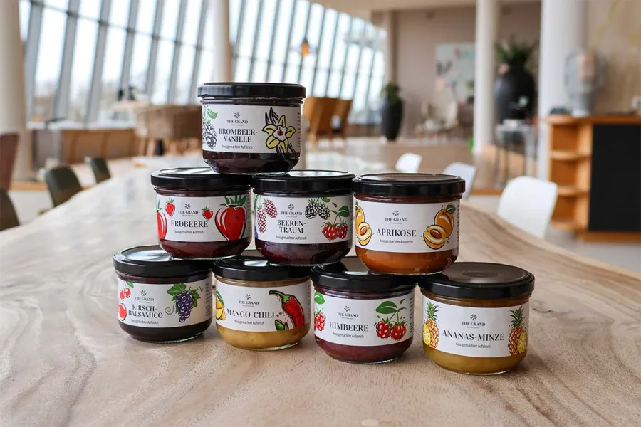 Übersicht von acht verschiedenen hausgemachten Marmeladen in Gläsern mit farbenfrohen Etiketten