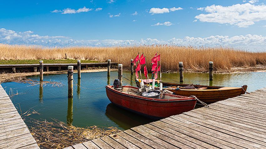 Zwei kleine Fischerboote mit roten Signalfahnen liegen an einem Holzsteg im Hafen von Althagen.