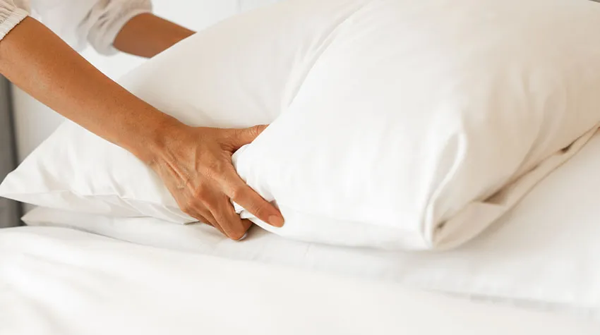Ein weißes Hotelkissen wird vom Housekeeping platziert.