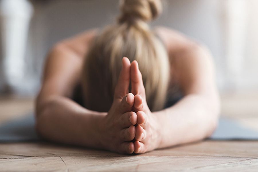 Person in ruhiger Yoga-Vorbeuge mit gefalteten Händen auf der Matte im THE GRAND Ahrenshoop.