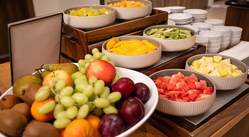 Ein Buffet mit frischem Obst, darunter Trauben, Äpfel, Pflaumen und geschnittene Früchte in Schalen.