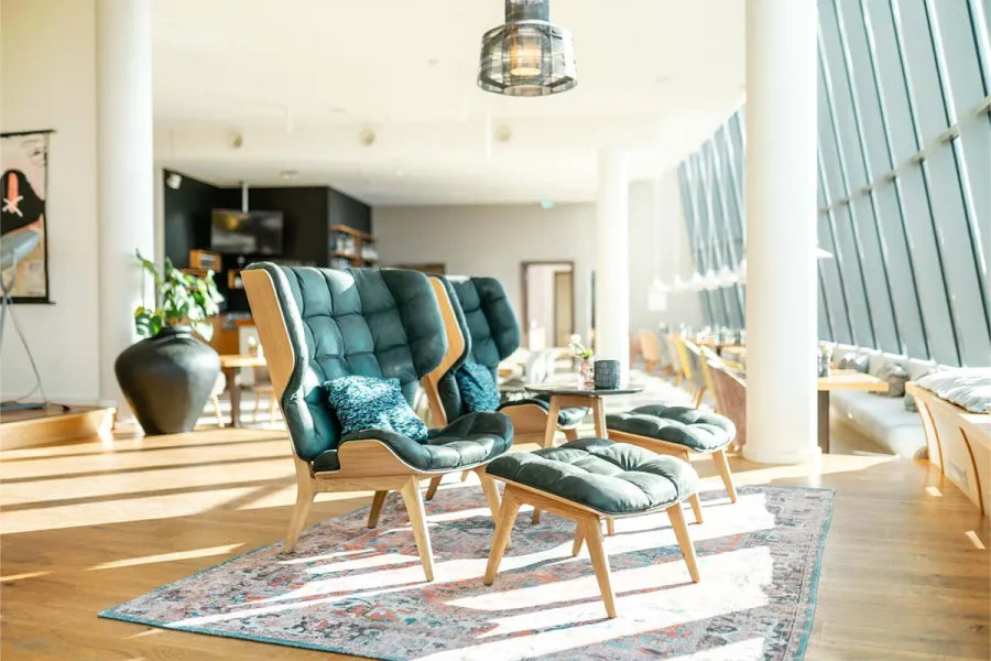 Helle Lounge mit Sesseln und Blick durch große Fenster im THE GRAND Ahrenshoop an der Ostsee.