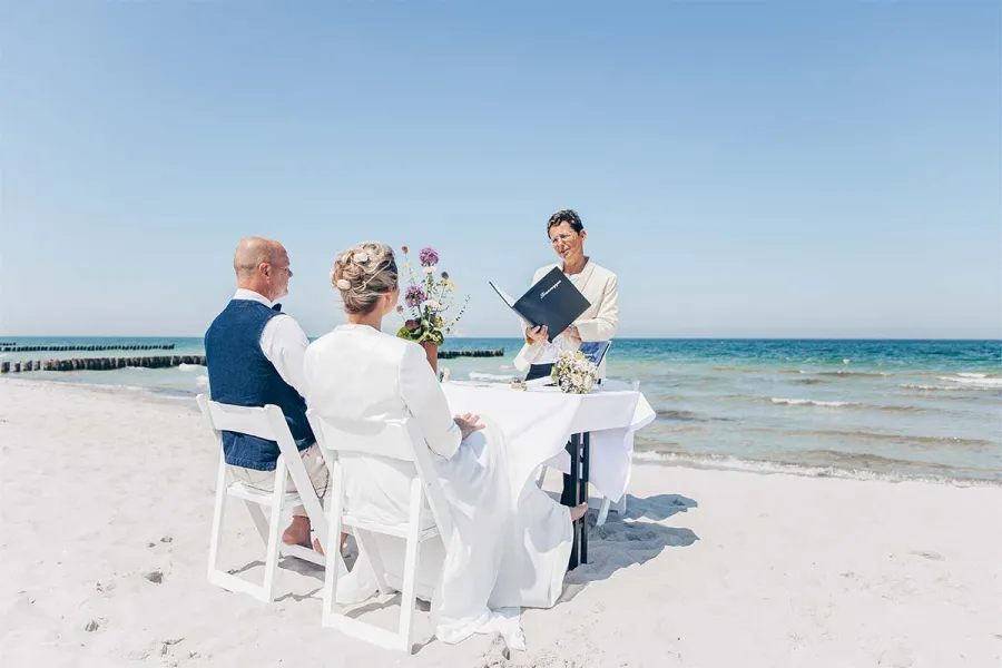 Brautpaar sitzt bei einer Trauung am Strand von Ahrenshoop mit Blick auf die Ostsee.