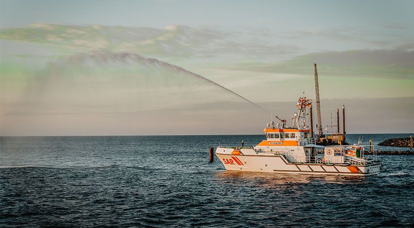 Schiff fährt auf blauem Meer, ein Wasserstrahl ragt in die Höhe.
