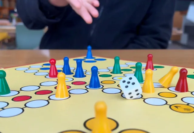 Nachaufnahme eines Brettspiels in bunten Farben im THE GRAND mit einem Kind im Hintergrund, der den Würfel wirft.