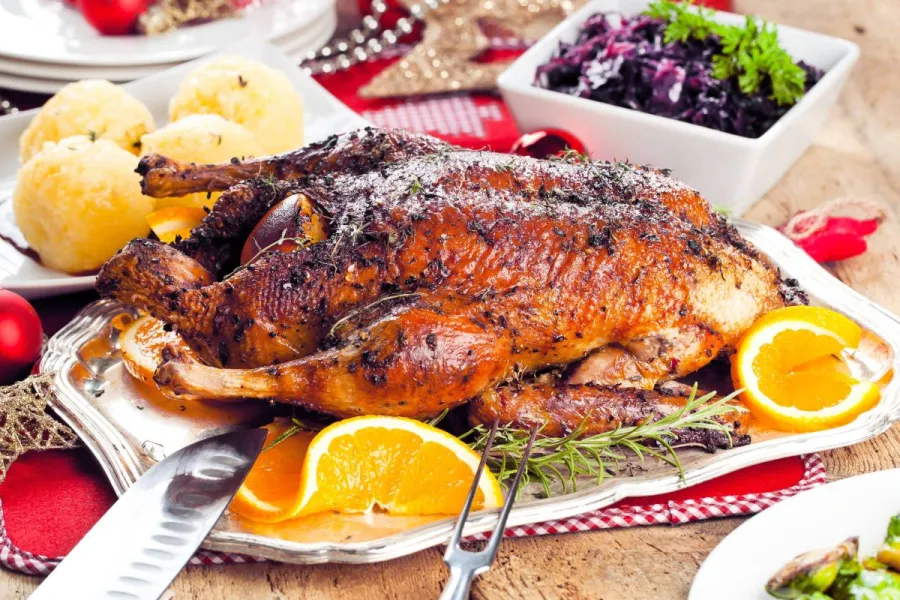 Knusprig gebratene Ente mit Kräuterkruste auf Silberplatte, dazu Kartoffelklöße, Rotkohl und Orangen, festlich gedeckt
