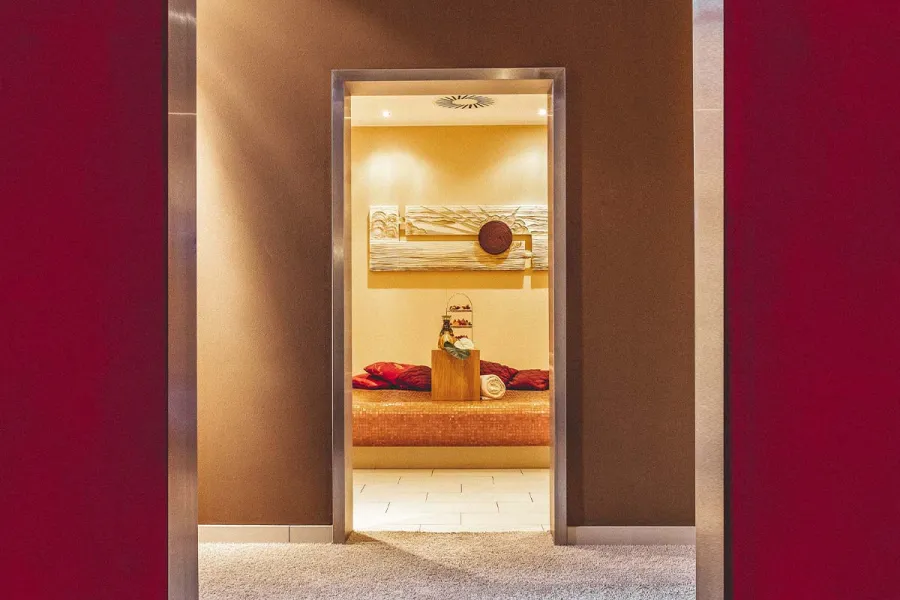 Blick durch eine Tür in einen warm beleuchteten Ruheraum mit gepolsterter Sitzbank im Spa an der Ostsee.