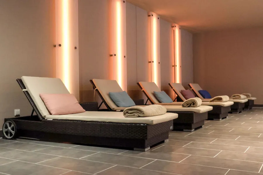 Moderne Ruheliegen mit Kissen und Handtüchern im warm beleuchteten Spa-Bereich des THE GRAND Ahrenshoop.