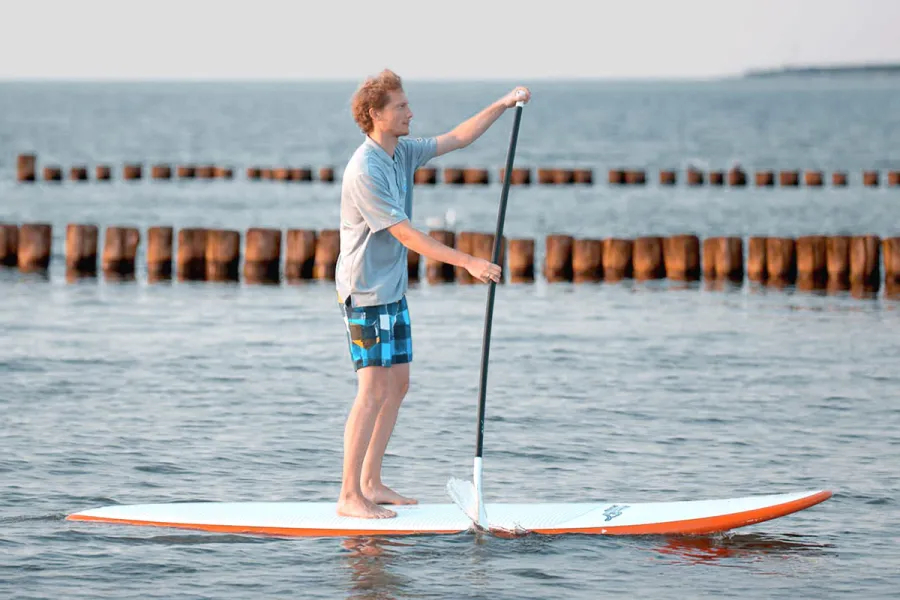 Mann steht barfuß auf SUP-Board und paddelt auf ruhiger Ostsee in Ahrenshoop.