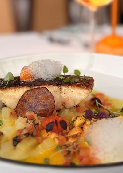 Saiblingsfilet im SEASIDE des THE GRAND Ahrenshoop mit Gemüsewürfeln, Kräutern und aromatischer Sauce auf tiefem Teller.