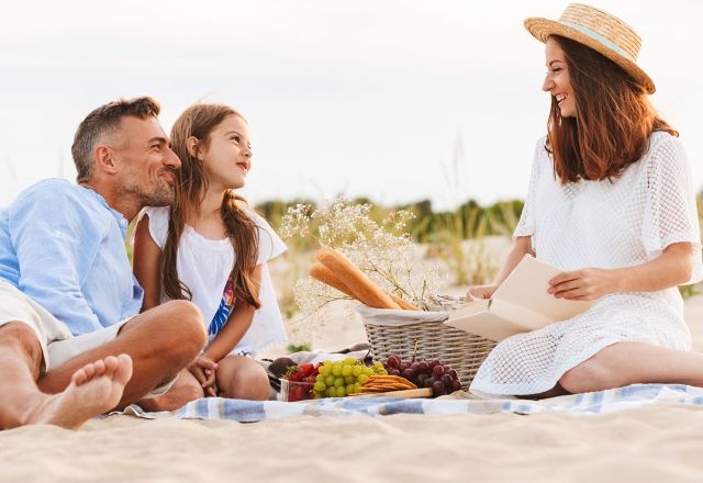 Familie genießt ein gemeinsames Picknick mit Burgern und Limo am Strand der Ostsee.