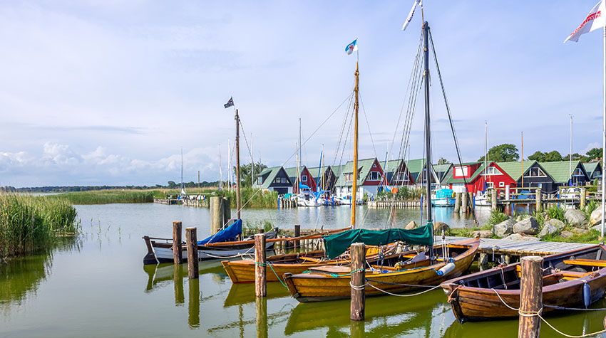Traditionelle Segelboote im Althagener Hafen vor bunten Reetdachhäusern