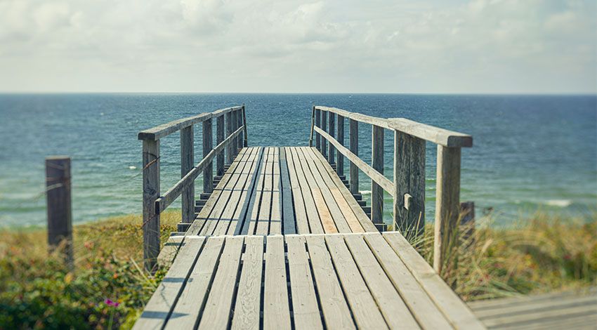 Langer Steg, der ans Wasser führt mit sanften Wellen im Hintergrund.