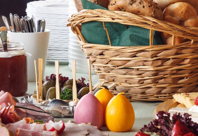 Ein festliches Osterfrühstück mit bunten Kerzeneiern im Mittelpunkt, begleitet von frischen Brötchen und einer Auswahl an Aufstrichen.
