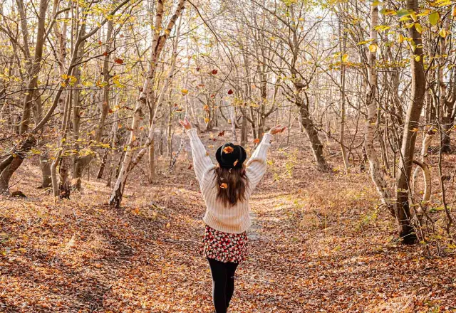 Im herbstlichen Wald spaziert eine Frau mit Hut, umgeben von buntem Laub.