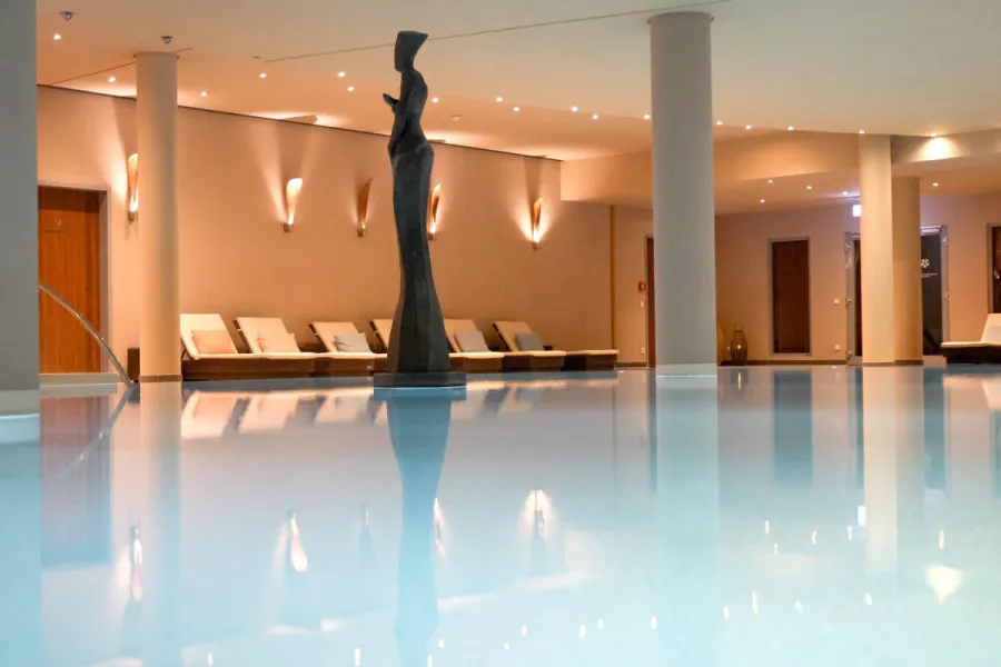 Beleuchteter Innenpool mit Skulptur in der Mitte und Ruheliegen entlang der Wand im Spa-Bereich an der Ostsee.