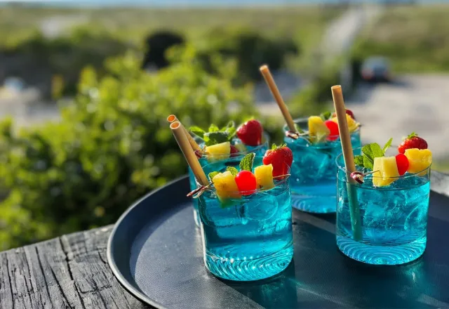 zwei blaue Cocktails, die auf einem Tablett stehen. Im Hintergrund sind Bäume und die Ostsee zu sehen