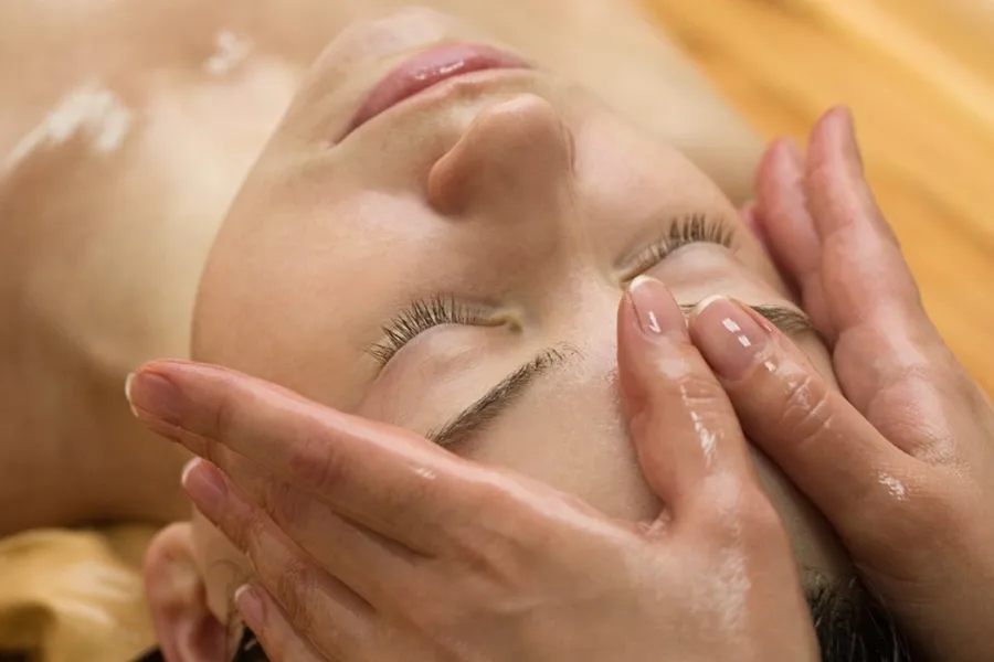 Eine Person erhält eine entspannende ayurvedische Gesichtsmassage mit Öl, durchgeführt von einem Therapeuten in ruhiger Wellness-Atmosphäre.