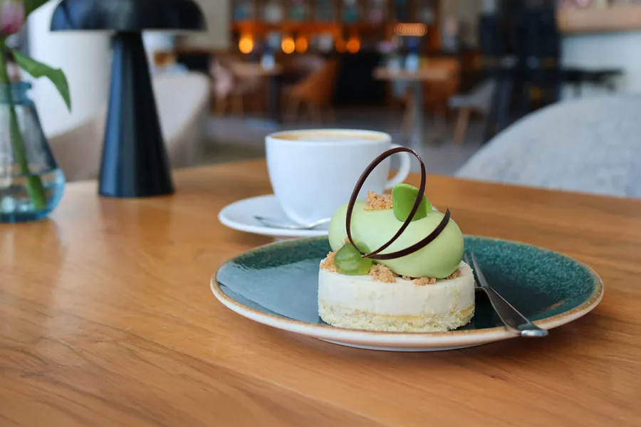 Kuchen auf einem Teller mit einer Tasse Kaffee im Hintergrund im THE GRAND Ahrenshoop.