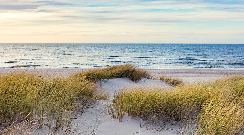 Die Ostsee mit Dühnen, Meer und leicht bewölktem Himmel.