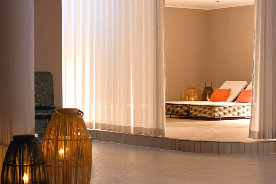 Gemütliche Liege hinter hellen Vorhängen im warm beleuchteten Spa-Bereich in Ahrenshoop.